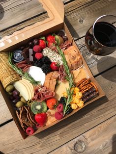 a wooden box filled with assorted cheeses and fruit next to a glass of wine