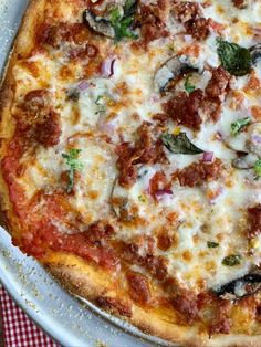 a pizza sitting on top of a metal pan covered in cheese and toppings next to a red checkered table cloth