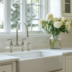 a white kitchen sink sitting under a window next to a vase with flowers in it