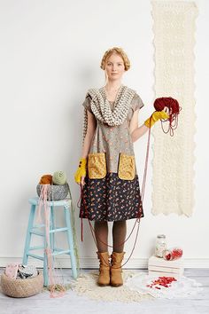 a woman standing in front of a white wall holding a red ball and some yarn