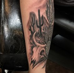 a black and white tattoo on the leg of a person with a deer skull in front of cacti