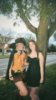 two young women dressed up in costumes posing for a photo next to a large tree