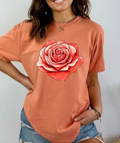 Elevate your wardrobe with this stunning vintage floral shirt featuring a bold, retro-inspired red rose graphic. Perfect for those who love the charm of cottagecore fashion and botanical prints, this flower t-shirt effortlessly combines style and comfort. Whether you're looking for a casual outfit or a unique gift for her, this floral aesthetic shirt is a perfect choice. Made from soft, high-quality fabric, this botanical tee is designed for all-day comfort and durability. The vibrant red rose design adds a pop of color, making it a standout piece in any collection. Whether you're dressing up for a day out in the garden or embracing your inner nature lover, this floral graphic tee is sure to become a favorite. Key Features: Premium Quality: Crafted from breathable, soft fabric that's perfe Summer Rose Print Short Sleeve T-shirt, Summer Short Sleeve T-shirt With Rose Print, Pink Rose Print Crew Neck T-shirt, Spring Rose Print Short Sleeve T-shirt, Summer Graphic Tee With Rose Print, Summer Cotton Tops With Rose Print, Spring Cotton T-shirt With Rose Print, Rose Print Tops For Spring, Short Sleeve Rose Print Tops For Summer