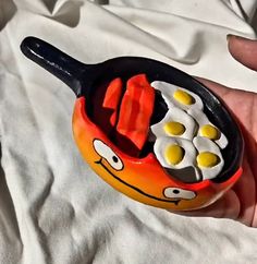 a hand holding a frying pan with eggs and sausages in it on a white sheet