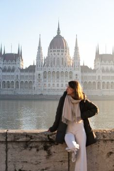 a woman leaning against a stone wall in front of a large building with spires