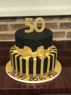 a 50th birthday cake decorated with black and gold stripes, bows and the number 50