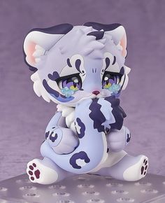 a white and blue cat figurine sitting on top of a purple surface with dots