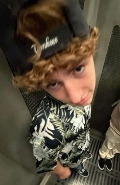 a young boy with curly hair wearing a hat and looking at the camera while standing on an escalator