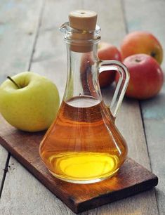 an apple cider and some apples on a wooden cutting board with oil in it