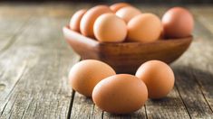 a wooden bowl filled with brown eggs on top of a table