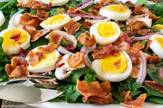 a salad with hard boiled eggs, bacon and spinach leaves on a white plate