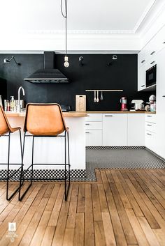 two brown chairs sitting in front of a counter top on a hard wood floor next to white cabinets