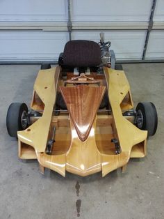 a wooden race car sitting in a garage next to a garage door and another vehicle behind it