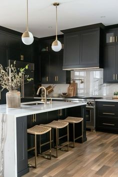 a large kitchen with black cabinets and white counter tops, gold accents on the island