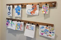 several drawings are hung on wooden pegs in front of a wall with calendars