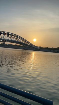 the sun is setting behind a bridge over water