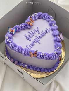 a heart shaped cake with purple frosting and butterflies on it in a cardboard box