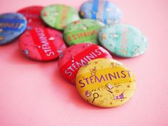 a bunch of buttons that are sitting on a pink surface with the words steminist written on them