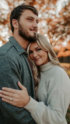 a man and woman hugging each other in front of trees