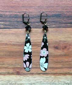 two pairs of black and white flowered earrings hanging from hooks on a wooden surface