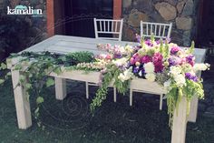 an outdoor table with flowers and greenery on it in front of a stone building