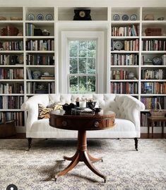 a living room filled with furniture and bookshelves next to a window in front of a white couch