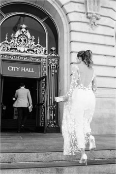 a woman is walking down the stairs in front of a city hall building with her back to the camera