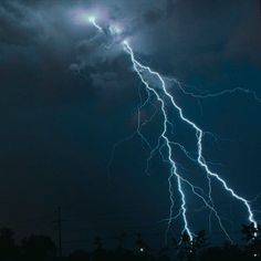 a lightning bolt is seen in the night sky above some trees and power lines on a cloudy day