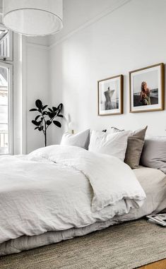 a white bed sitting next to a window with pictures on the wall above it in a bedroom