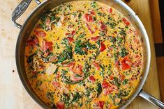 an omelet with tomatoes, spinach and cheese in a pan on a cutting board