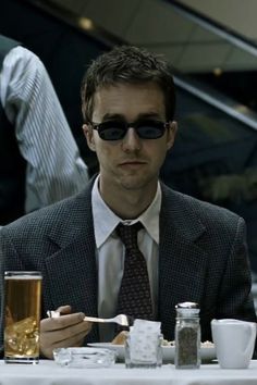 a man sitting at a table with food and drinks in front of him, wearing sunglasses