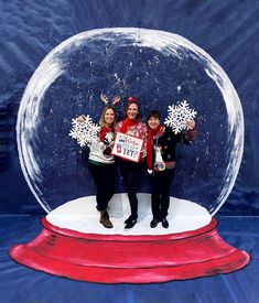 two women and a boy standing in front of a snow globe with christmas decorations on it