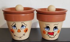 two pots with faces painted on them sitting on a table next to each other and one has an egg in it