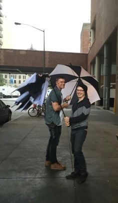 two people standing on the sidewalk holding umbrellas