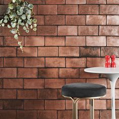 a white table and two stools in front of a brick wall with a potted plant