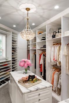 a walk in closet with chandelier, drawers and shelves filled with clothes on hangers