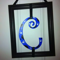 the letter c is painted blue and has paw prints on it, hanging from a black frame