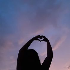 the silhouette of a woman making a heart shape with her hands in front of a purple sky