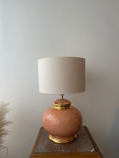 a lamp sitting on top of a wooden table next to a white vase with a gold rim