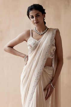 Ivory saree with zari thread, cutdana, sequin embroidery in floral pattern on border. Paired with sleeveless embroidered blouse.
Components: 2
Pattern: Embroidery
Type Of Work: Zari Thread, Cutdana, Sequin, Floral
Neckline: Leaf neck
Sleeve Type: Sleeveless
Fabric: Pure Georgette
Color: Ivory
Other Details: 
Back deep square neck
Pearl drops on pallu
Occasion: Reception - Aza Fashions Ivory Sari, Floral Thread Embroidery, Stylish Saree, Blouse Yoke, Ethnic Suit, Border Saree, Desi Style, Stylish Sarees, Thread Embroidery