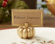 a place card holder with a small gold pumpkin on it, sitting on a plate