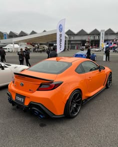 an orange toyota sports car parked in a parking lot next to other cars and people