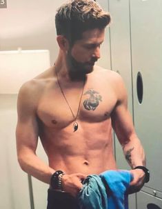 a shirtless man is looking in the mirror with his hand on his pants and holding a blue towel