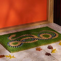 a door mat with a snake on it in front of an orange wall and leaves