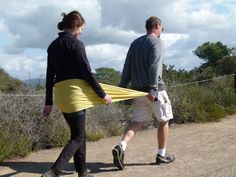 a man and woman walking down a dirt road with a yellow blanket on their back