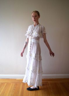 An antique Edwardian era from the 1910s. It is a really unique dress with embroidered daisies. It also has a ruffled overlayer on the bodice, a skirt with tiered ruffles, inset lace, and lace trim. The dress has decorative crochet-covered buttons and fastens with snaps and hook and eyes up the front. The dress has two kinds of fabric -- a lightweight cotton as well as a cotton net. Size: xs to small Bust: up to 34" Waist: 26" Hip: 42" (meant to drape) Length: 54-55" Condition: Very good. Faint yellowing on front waistband that didn't completely lift when I cleaned dress. A handful of small hand repairs -- the two pictured are on the netting above back waist and on the back shoulder. None of the flaws jump out at you, and the dress presents beautifully. Fitted White Vintage Dress With Ruffles, White Fitted Vintage Dress With Ruffles, White Fitted Ruffled Vintage Dress, Fitted Vintage Victorian Dress With Cancan, Fitted Vintage Victorian Dress With Attached Cancan, Fitted Victorian Dress With Attached Cancan, 1920s Style Dresses For Vintage Summer Events, 1920s Style Summer Dresses For Vintage Events, Spring Victorian Vintage Dress