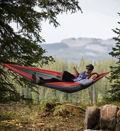 a man laying in a hammock with his feet up on the ground next to trees