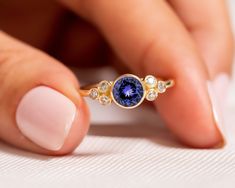 "14K Gold Natural Tanzanite Ring/Rose Gold Tanzanite Engagement Ring/Something Blue/Bezel Set Diamond Cluster Wedding Ring/Anniversary Gift   ★ ★ ★ ★  CUSTOM/DUTY-FREE SHIPPING WORLDWIDE, BUYERS DON'T HAVE TO PAY ANY CUSTOM FEES WHILE IMPORTING ★ ★ ★ ★  Details Made to order Material: 14k/18k Gold Color Options: Yellow Gold, White Gold, Rose Gold ★ Center Stone Tanzanite, Round Size: 6 mm  Approx Weight (Ct): 0.75 ★ Accent Stones Diamond/Moissanite, Round Size: 1.8mm * 6 Nos Approx Weight (Ct): 0.15 ★ 100% Natural Diamond and Gemstones ★ Diamond: Round Brilliant cut, G-H Color, SI Clarity ☂ Shipped with Insured Shipping within 4-7 business days. ➦ 100% Free Returns. ➦ Our Jewelry comes with a Lifetime Warranty. (Stone Replacement not included) ✈ We offer free EXPRESS shipping across the wo Cluster Wedding Ring, Tanzanite Engagement Ring, December Birthstone Ring, Diamond Cluster Engagement Ring, Tanzanite Diamond, Natural Gemstone Jewelry, Tanzanite Ring, Tanzanite Gemstone, Bezel Set Diamond