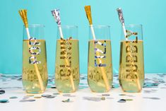 three champagne glasses with gold straws and confetti sticks in them on a table