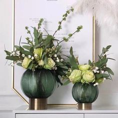 two green vases with white flowers and greenery